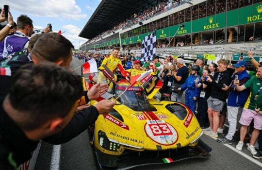 The AF Corse team and drivers celebrate their historic 2025 Le Mans victory with the #83 Ferrari 499P, surrounded by fans and a checkered flag.