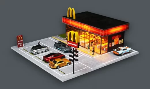 A detailed 1/64 scale diorama of a modern McDonald's restaurant at night, with LED lighting, showcasing several diecast model cars in a car meet scene.